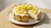 Une part généreuse de charlotte Piña Colada crémeuse avec des biscuits Maria et des morceaux d'ananas frais sur le dessus.